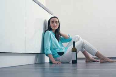 Mutfakta bir bardak ve bir şişe kırmızı şarap ile oturan duygusuz bir bayan. kopya alanı.