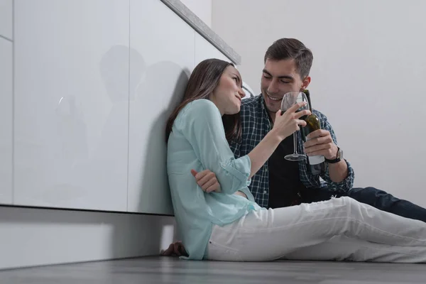 The couple sits on the floor of the white kitchen and drinks red wine, celebrate the housewarming, the end of the week.