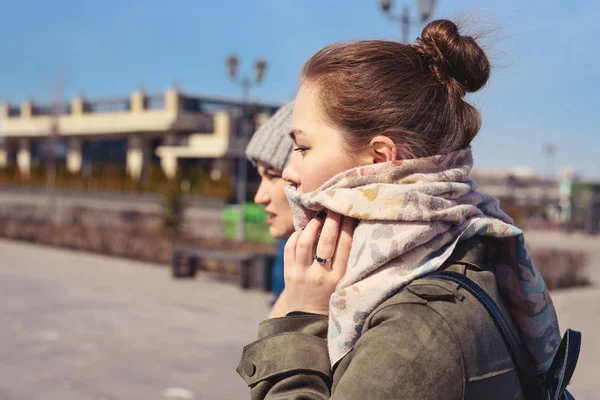 Side portrait of two young girls in a coat, scarf and hat, cold wind.