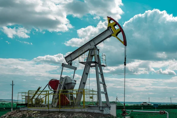 Oil pump tower in the field with green grass with blue cloudy sky.