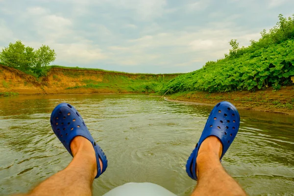 close-up of men\'s feet in rubber sandals on a catamaran on the background of the river, outdoor activities.