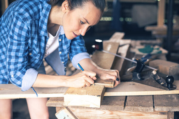 Side view of a woman carpenter draws on wooden board cut line