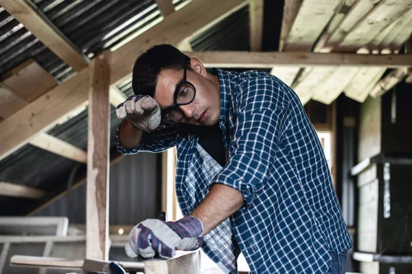 Man in goggles and wipes his forehead from sweat when handling wooden boards planer, heavy manual labor, handyman, diy