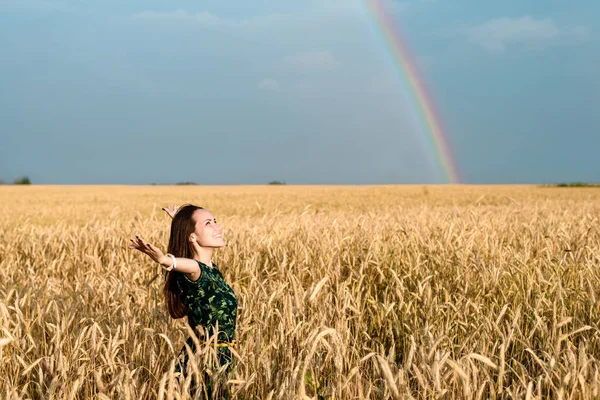 Freedom. Woman with open hands on a wheat field on a background of rainbows