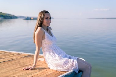 Beyaz sundress iskeleye günbatımında oturan genç esmer