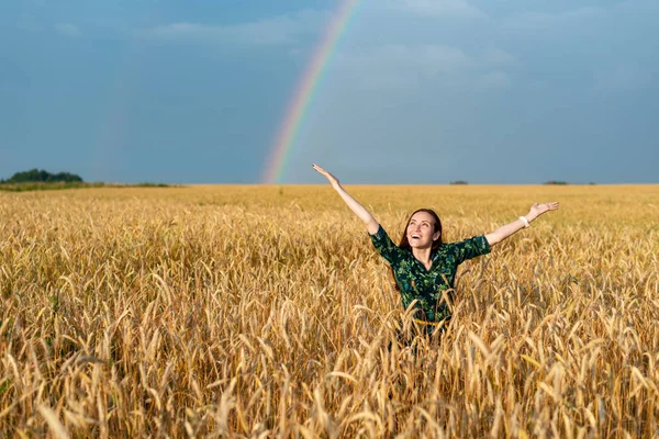 Happy woman in field with wheat hands in sides.