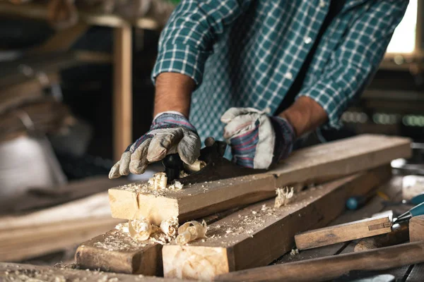 Close-up of the hands of a gloved carpenter with a hand planer handles wood.