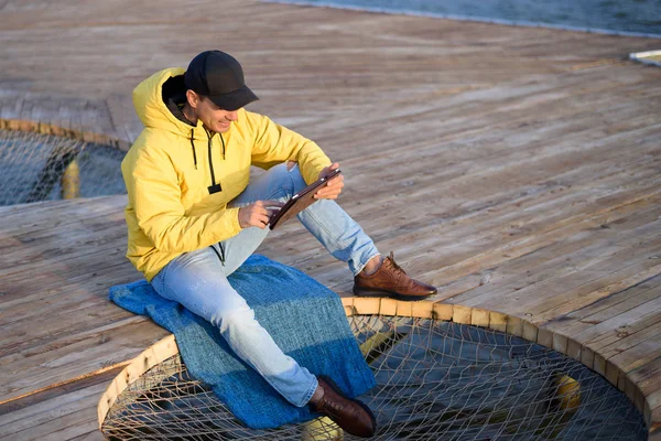 Guy Yellow Jacket Black Cap Sitting Pier Tablet — Stock Photo, Image
