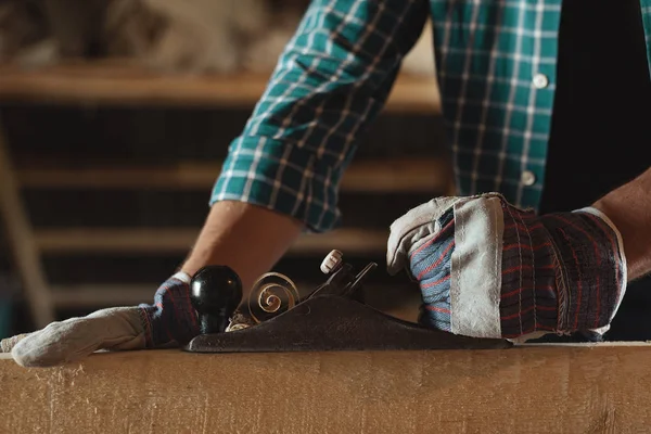 Erkekler Close-up odun kesmek el uçak ile çalışma eldiven eller. ağaç işleri, çatı kaplama, inşaat, endüstriyel arka plan