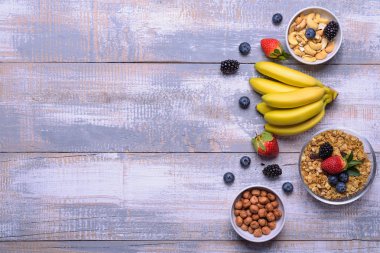 Sağlıklı kahvaltı maddeler, gıda çerçeve. Müsli, fındık, meyve, çilek, muz ahşap rustik arka plan üzerinde. Görünümü en çok, uzay kopyalayın. Sağlıklı gıda kavramı