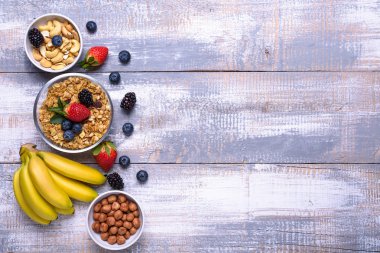 Sağlıklı kahvaltı maddeler, gıda çerçeve. Müsli, fındık, meyve, çilek, muz ahşap rustik arka plan üzerinde. Görünümü en çok, uzay kopyalayın. Sağlıklı gıda kavramı