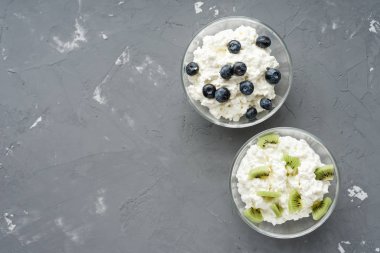 İlk kopya alanı, sağlıklı kahvaltı kavramı çimento zemin üzerine iki kase süzme peynir, yaban mersini ve kivi ile göster