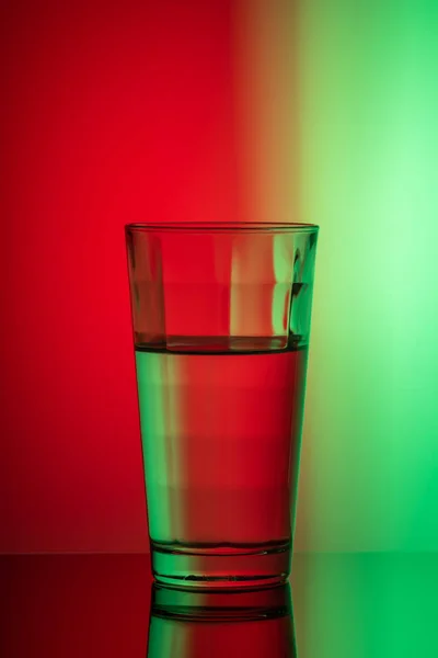 Gambar vertikal dari kaca air pada latar belakang merah-hijau — Stok Foto