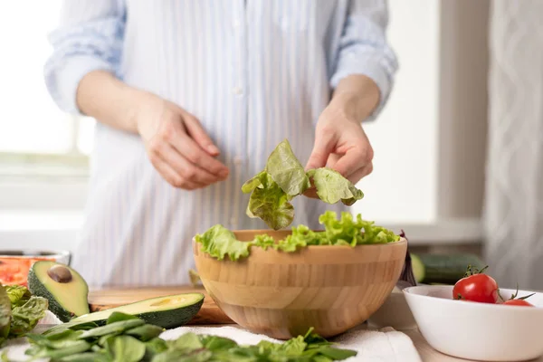 Mujer en una camisa azul preparando ensalada de verduras, lechuga laica —  Fotos de Stock