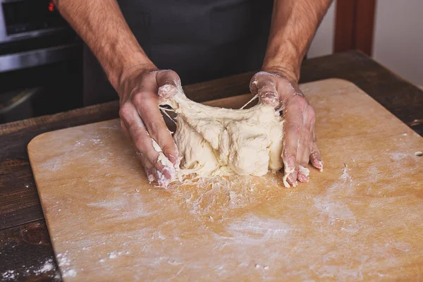 Le mani degli uomini impastano la pasta sul tavolo in cucina — Foto Stock