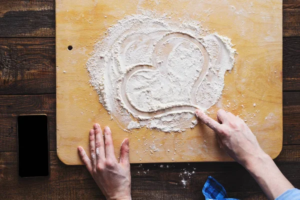 women's hands draw heart on flour in the kitchen
