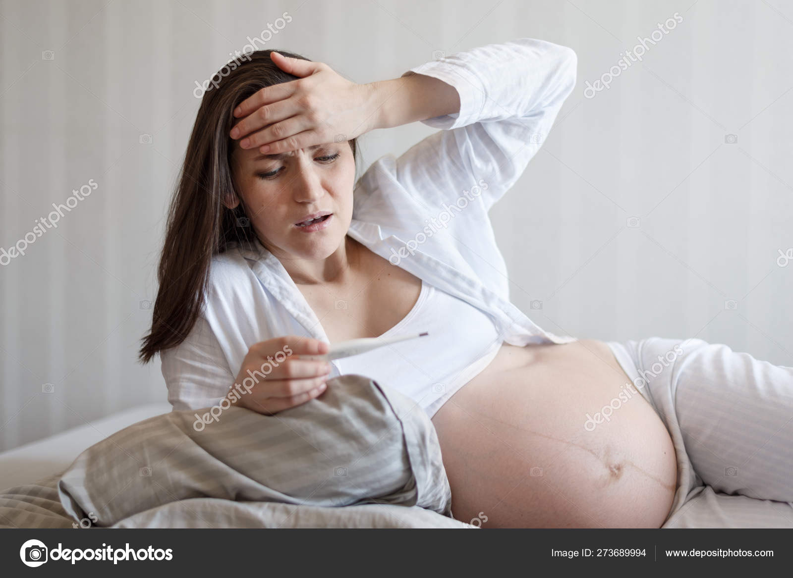 Frontal Portrait Of A Pregnant Woman Lying In Bed With A Thermometer Holding Her Head Temperature Cold Flu During Pregnancy Stock Photo Image By C Rasselbor 273689994