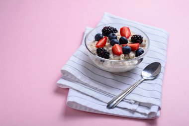 Glass bowl with oatmeal and berries on pink background