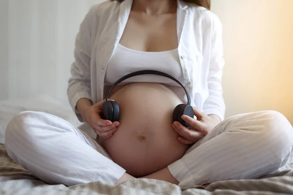 Musique pour enceinte. gros plan de la femme enceinte avec casque sans fil s'applique au ventre — Photo