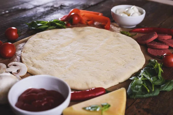 Raw rolled pizza dough with ingredients on edges