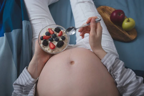 ベリーとオートミールを食べるベッドで妊娠中の女性のクローズアップ — ストック写真