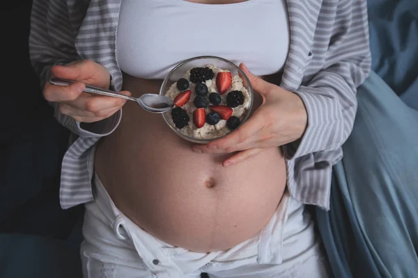 Primer plano de la mujer embarazada en la cama comiendo avena con bayas — Foto de Stock