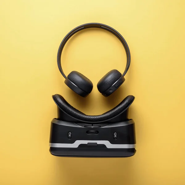 Konst design prylar på gul bakgrund, trådlösa hörlurar och VR-glasögon — Stockfoto