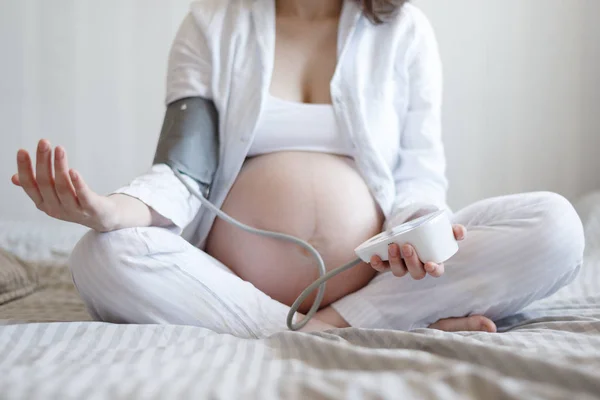 Hamile bir kadının karnının frontal yakın çekim, bir yüz olmadan, bir sphygmomanometer ile kan basıncını ölçer