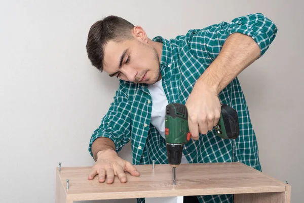 Vista frontal de un hombre en una camisa con un destornillador eléctrico recoge muebles — Foto de Stock