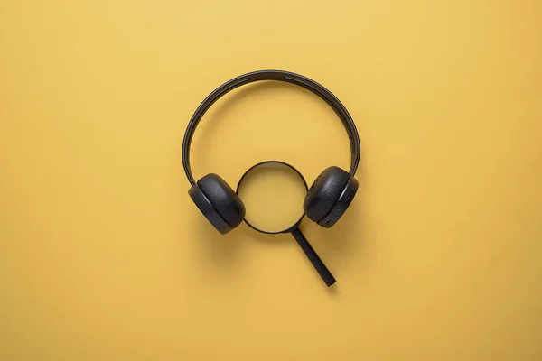 Begreppet Sök i nätverket, musik, inspiration. Förstorings glas med trådlösa hörlurar på gul bakgrund — Stockfoto