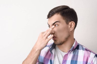 Genç adam hoş olmayan bir koku, gri arka planda portre elini ile burnunu kelepçeler