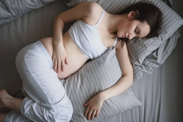 Портрет молодой беременной женщины, спящей в постели с подушками — стоковое фото