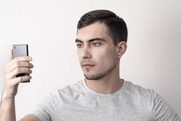 Caucasian man in t-shirt and smartphone in hand uses face recognition — Stock Photo, Image