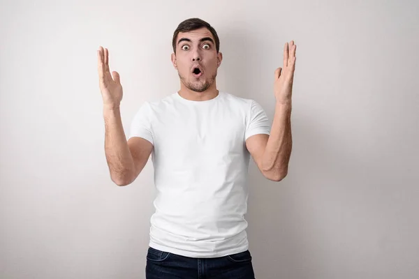Portrait of shocked, surprised young guy shows hands size in white empty t-shirt for design. — Stock Photo, Image
