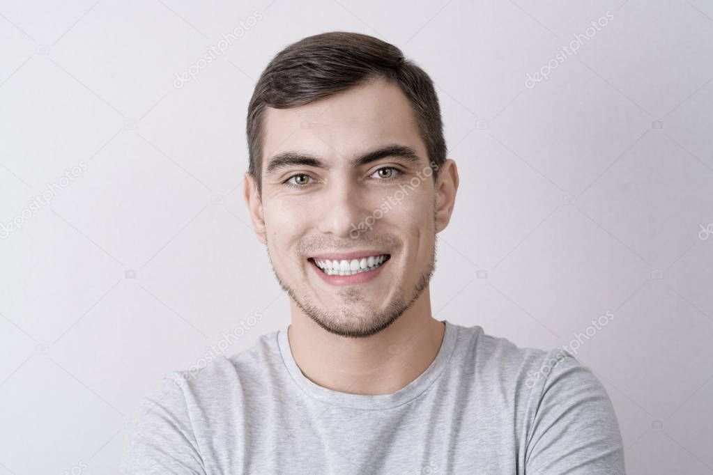 Close-up portrait of European man with perfect white smile isolated on grey background