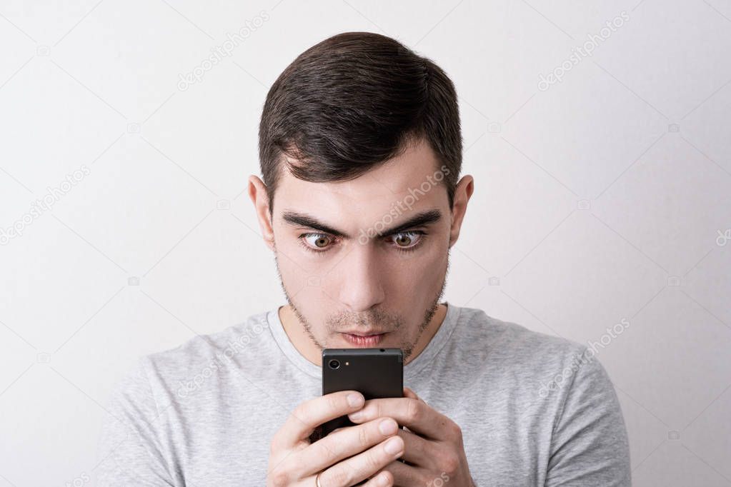 Funny portrait of man with a smartphone in his hands looking at the screen with bulging eyes