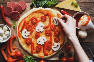 Kadın eli üst görünümü yuvarlak bir pizza hamuru üzerinde mantar ve kiraz domates koyar