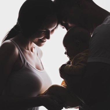 Genç bir ailenin silueti, kucağında bir bebek tutan bir adam, gelin gülümseyerek önünde duruyor