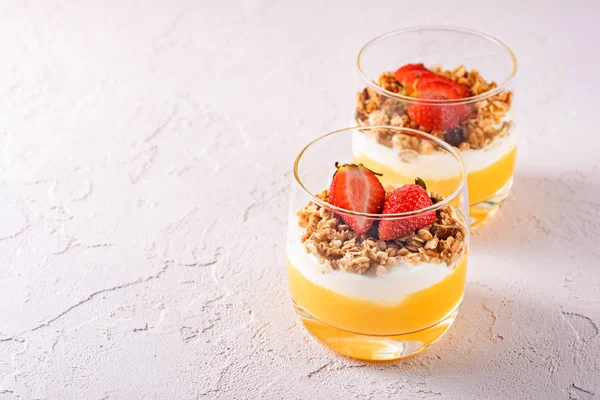 Deux verres en verre avec desserts végétariens à base de smoothie à la mangue, yaourt grec, granola et fraise avec espace de copie — Photo