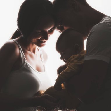 Siluet genç bir ailenin yaratıcı aile portresi, anne kollarında sarılma ve gülümseyerek yeni doğmuş bir bebek tutan ebeveynler