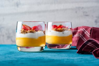 Turkuaz dokulu arka plan üzerinde mango, yoğurt, pişmiş müsli ve çilek iki tatlılar Ön görünümü