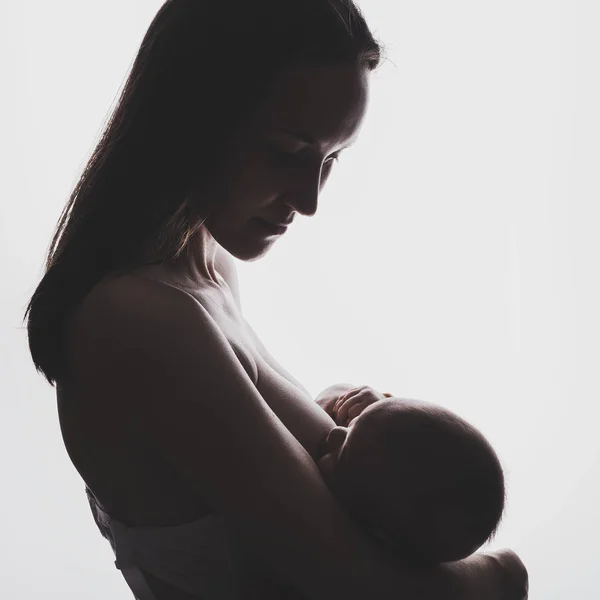 Authentic silhouette of a young woman with a newborn baby in her arms breastfeeding — Stock Photo, Image