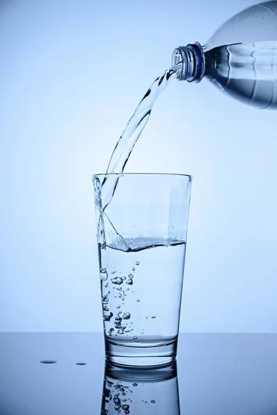 Imagen vertical en una taza de vidrio alta verter agua limpia de una botella de plástico — Foto de Stock