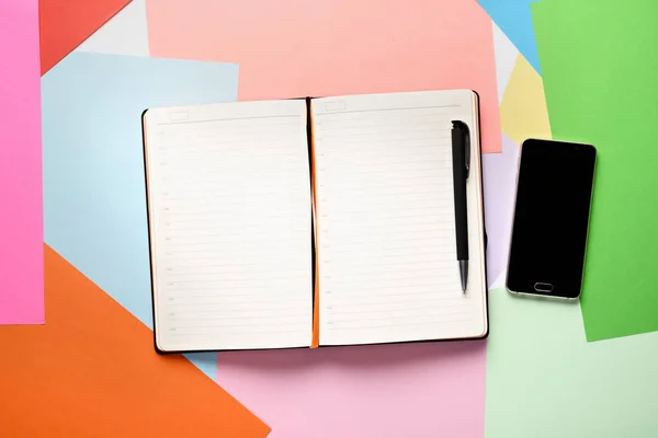 Vista superior del bloc de notas de papel abierto con lápiz y teléfono inteligente sobre un fondo de color — Foto de Stock