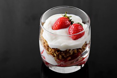 siyah arka plan üzerinde krem şanti, granola ve çilek ile tatlı
