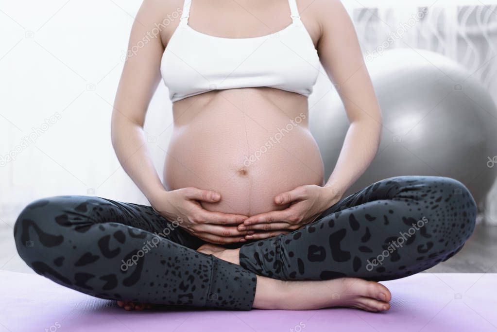 pregnant woman with hands on her stomach sitting on sports Mat