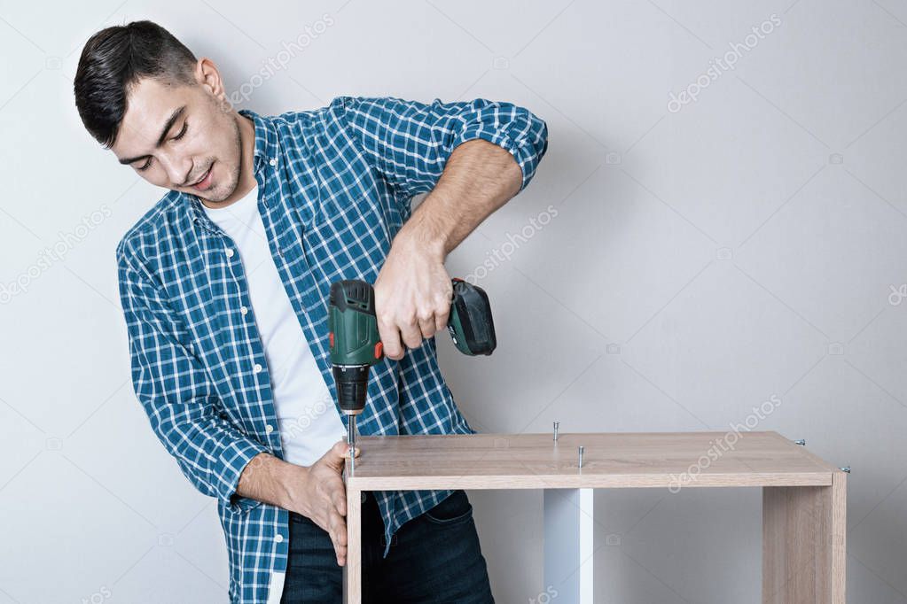 Confident smiling European man collects furniture with an electric screwdriver with a copy of the space