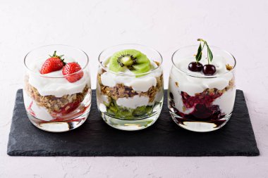 açık pembe arka plan üzerinde siyah taş üzerinde çırpılmış süzme peynir, granola, çilek, kiraz ve kivi ile meyve ve berry tatlı