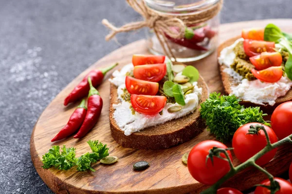 Kanapki z serem ricotta i pesto z pomidorkami wiśniowym, chilli i ziołami na drewnianej płycie — Zdjęcie stockowe