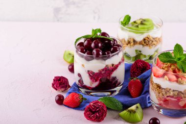 Pembe arka planda çeşitli çilek tatlılar, granola farklı tatlılar ile üç bardak, krem şanti, çilek, kivi, kiraz
